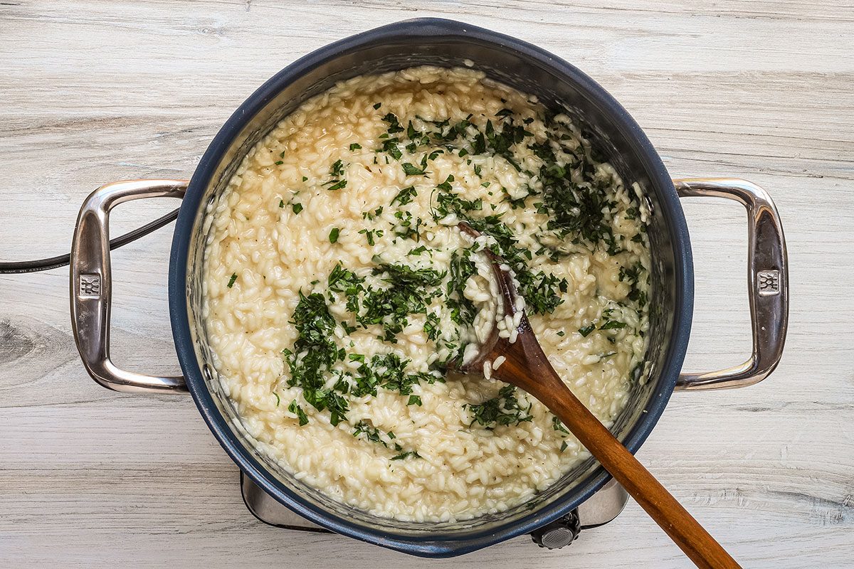 Stirring parsley into a pot of Parmesan risotto.