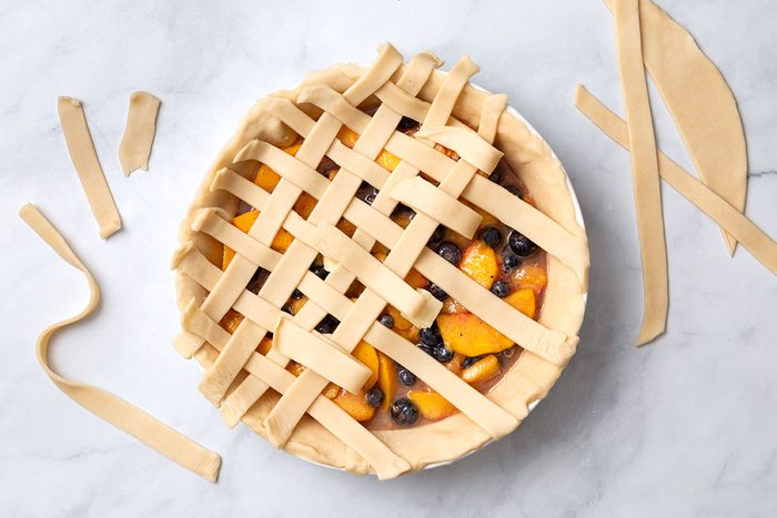 Strips of pie dough woven into a lattice pattern on top of the pie for step four of Peach and Blueberry Pie recipe for Taste of Home