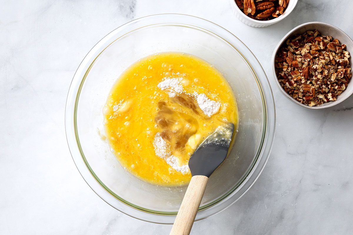 Sugar, flour and salt being mixed with honey, eggs, butter and vanilla in a mixing bowl for step two of Pecan Pie Without Corn recipe for Taste of Home