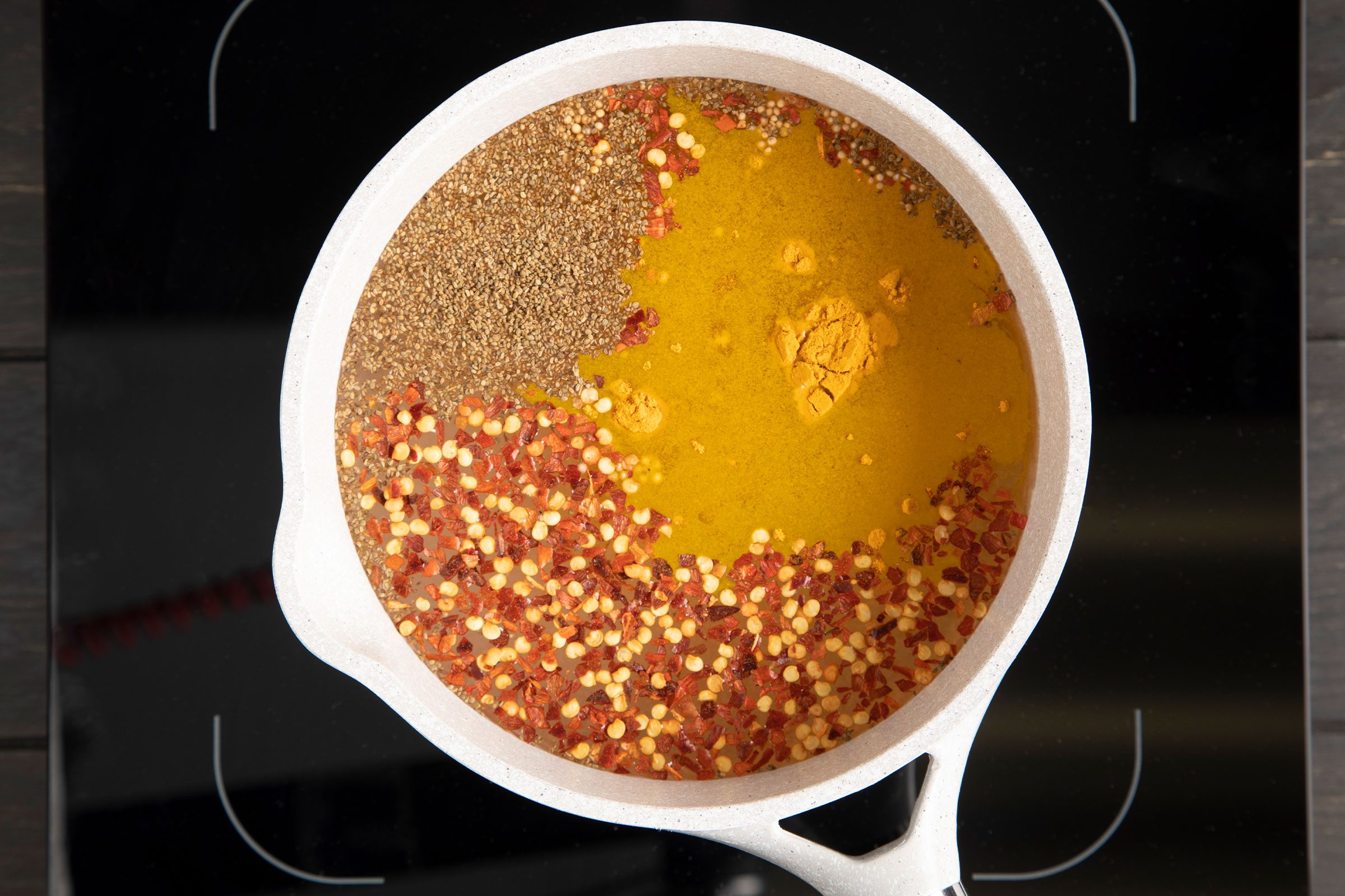 spices floating in a brine for pickled cauliflower in a pan on a stovetop