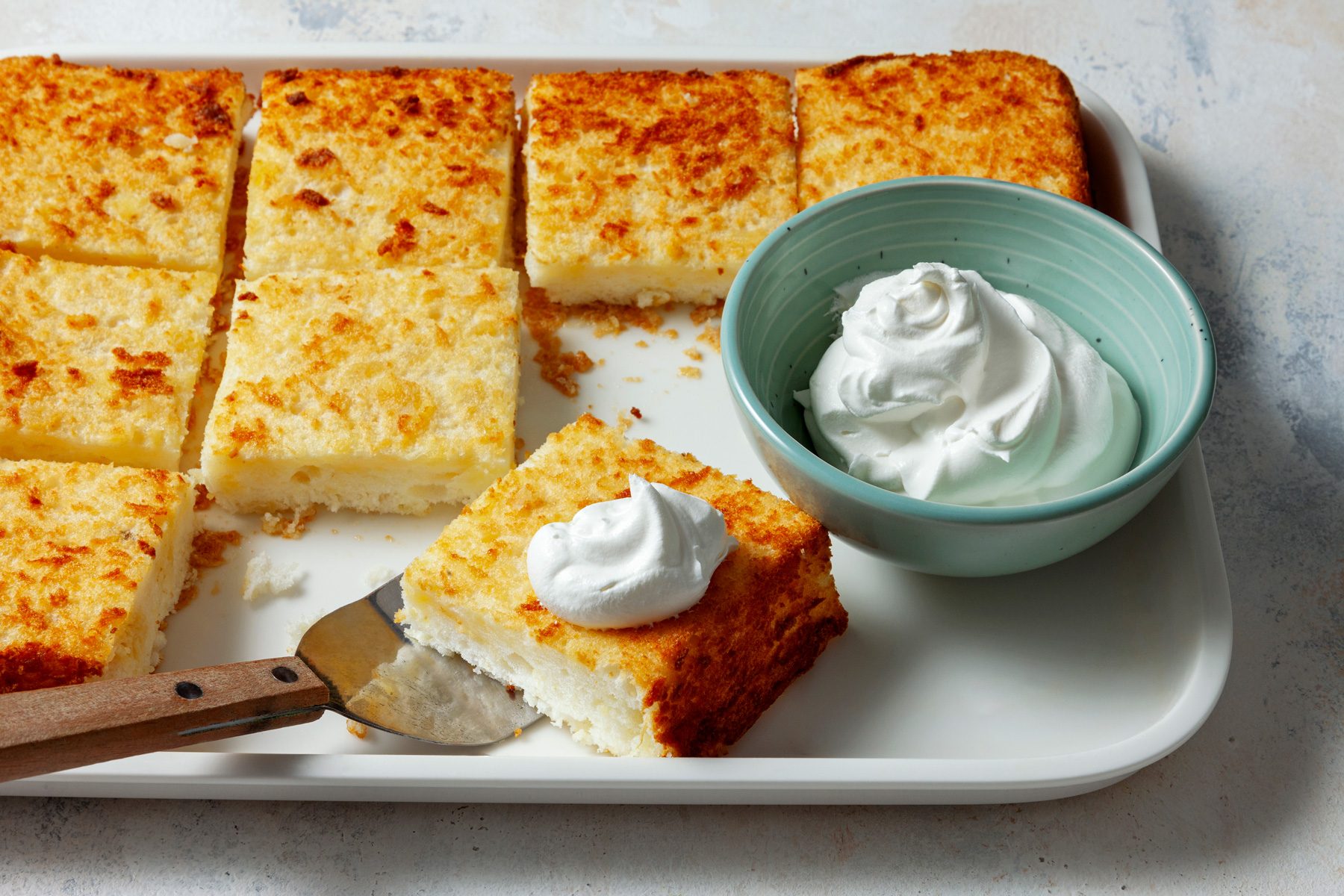 A three-quarter shot captures a slice of Pineapple Angel Food Cake, elegantly topped with whipped cream.
