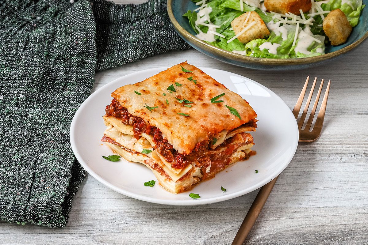 Pizza Lasagna on a plate with a Caesar salad in the background.