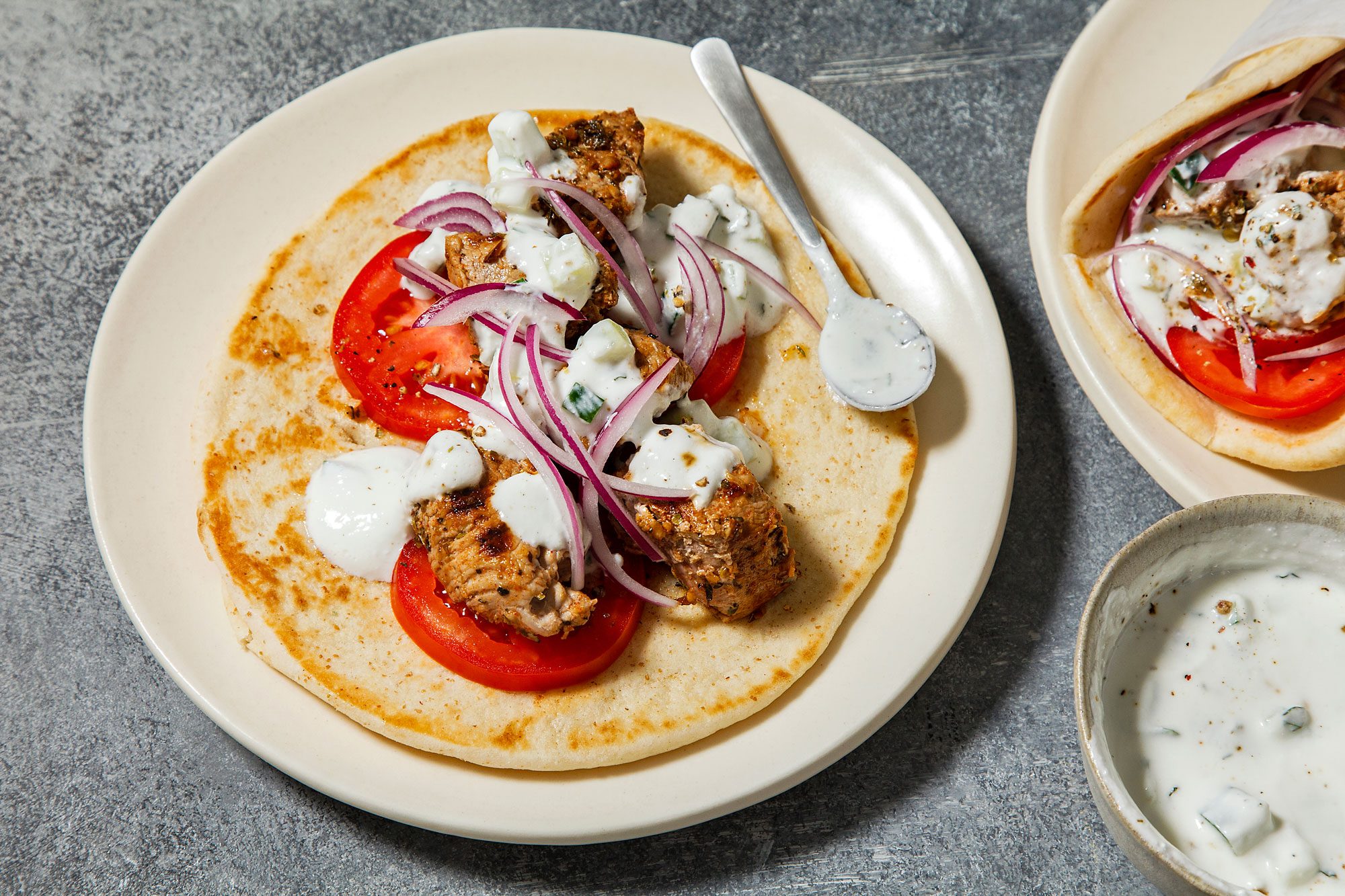 overhead shot of two plates of Greek gyros, Each plate contains a pita bread wrap filled with grilled chicken skewers, sliced tomatoes, red onion, and tzatziki sauce, The chicken is cooked to a golden brown color and is seasoned with herbs and spices, The tzatziki sauce is creamy and white, and the vegetables are fresh and colorful;