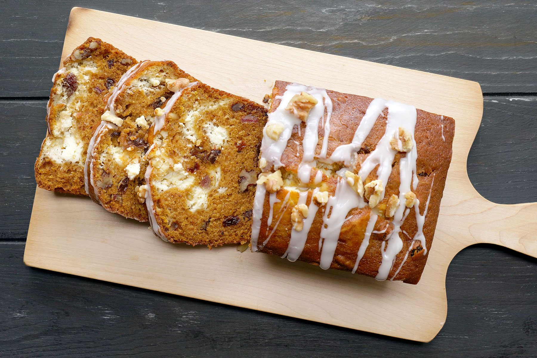 Slices of raisin bread with icing and walnuts on top are laid out on a wooden board.