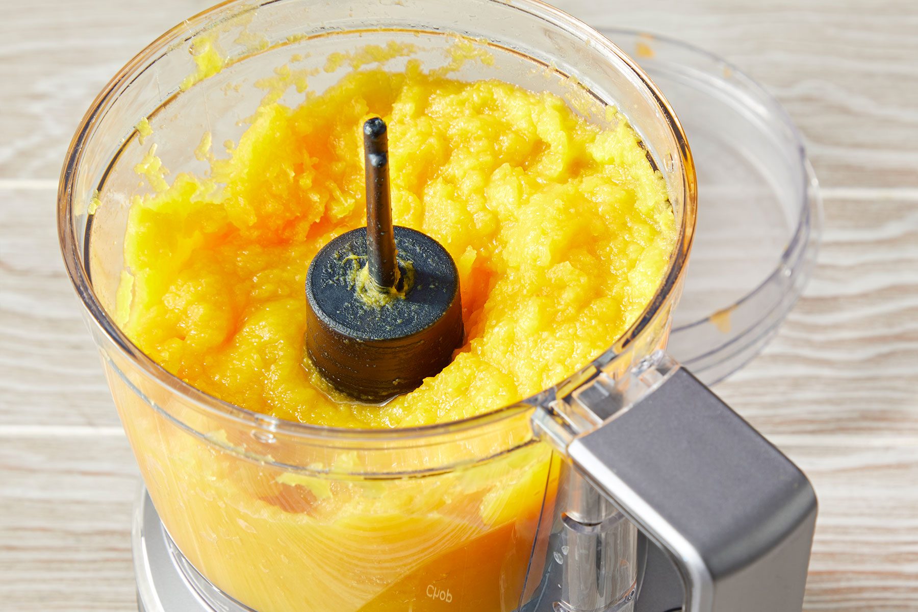 Pureed pumpkin in a food processor on a wooden surface.