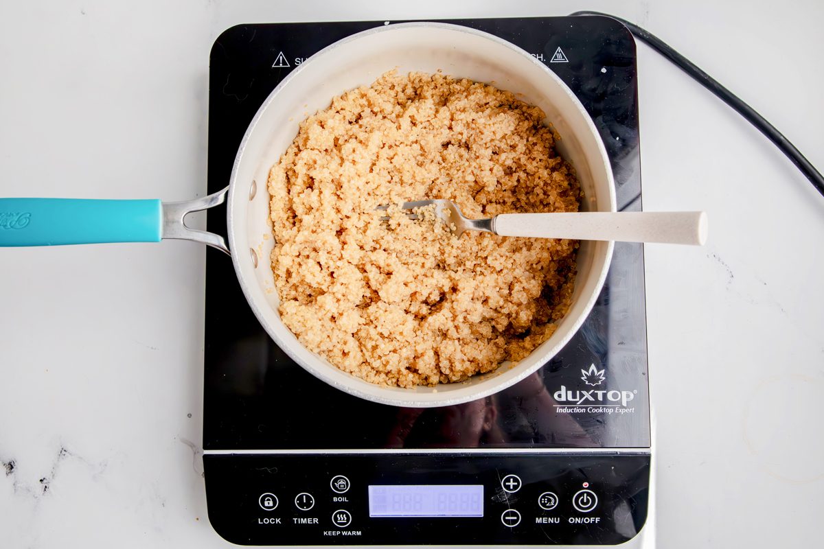 Overhead shot for Taste of Home Quinoa with Vegetables, quinoa being fluffed with a fork over an induction cooktop.