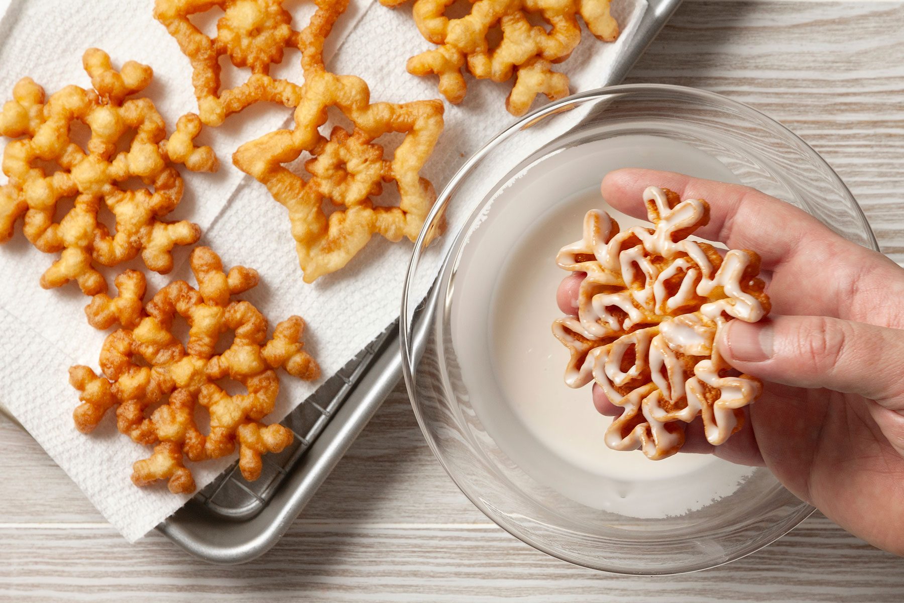A hand can be seen holding one cookie dipped in icing next to a wire rack with more cookies.