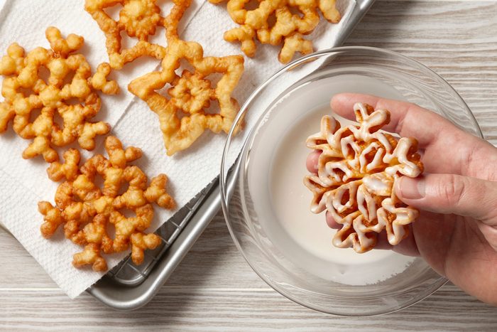 A hand can be seen holding one cookie dipped in icing next to a wire rack with more cookies.