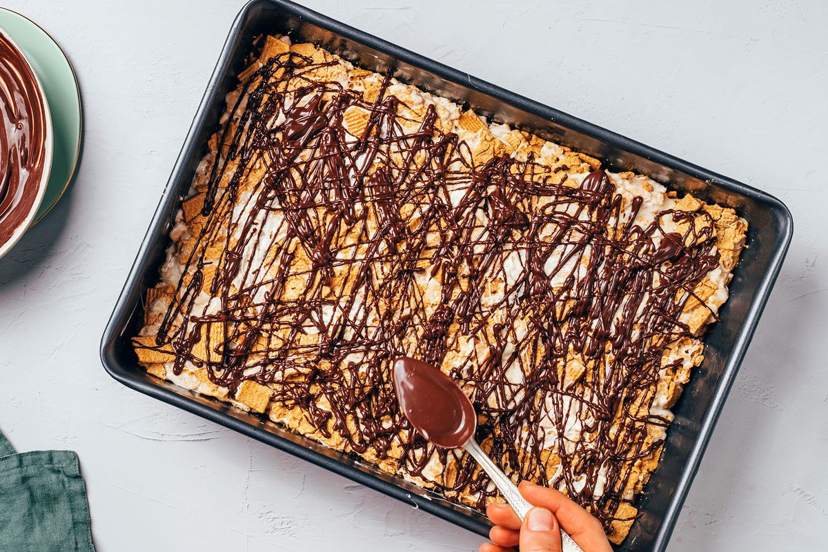 Melted milk chocolate being drizzled over the marshmallow cereal base for Smores Bars recipe by Taste of Home