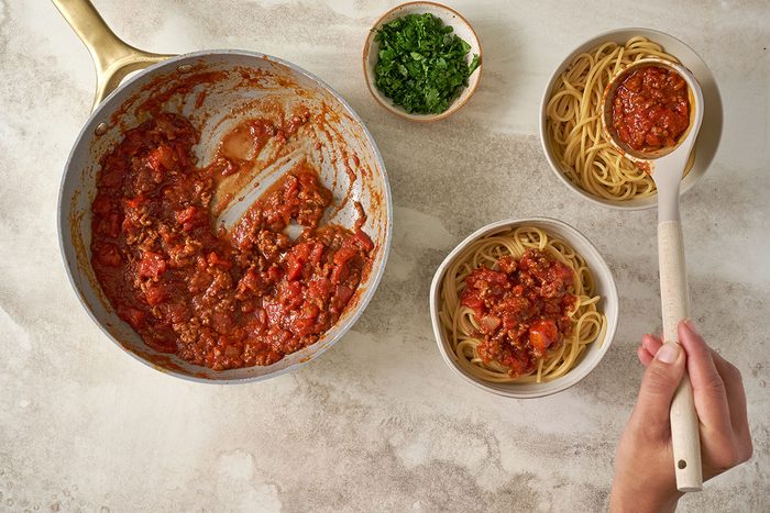 Cooked spaghetti plated, being topped with the salsa sauce for Taste of Home's Salsa Pasta recipe.