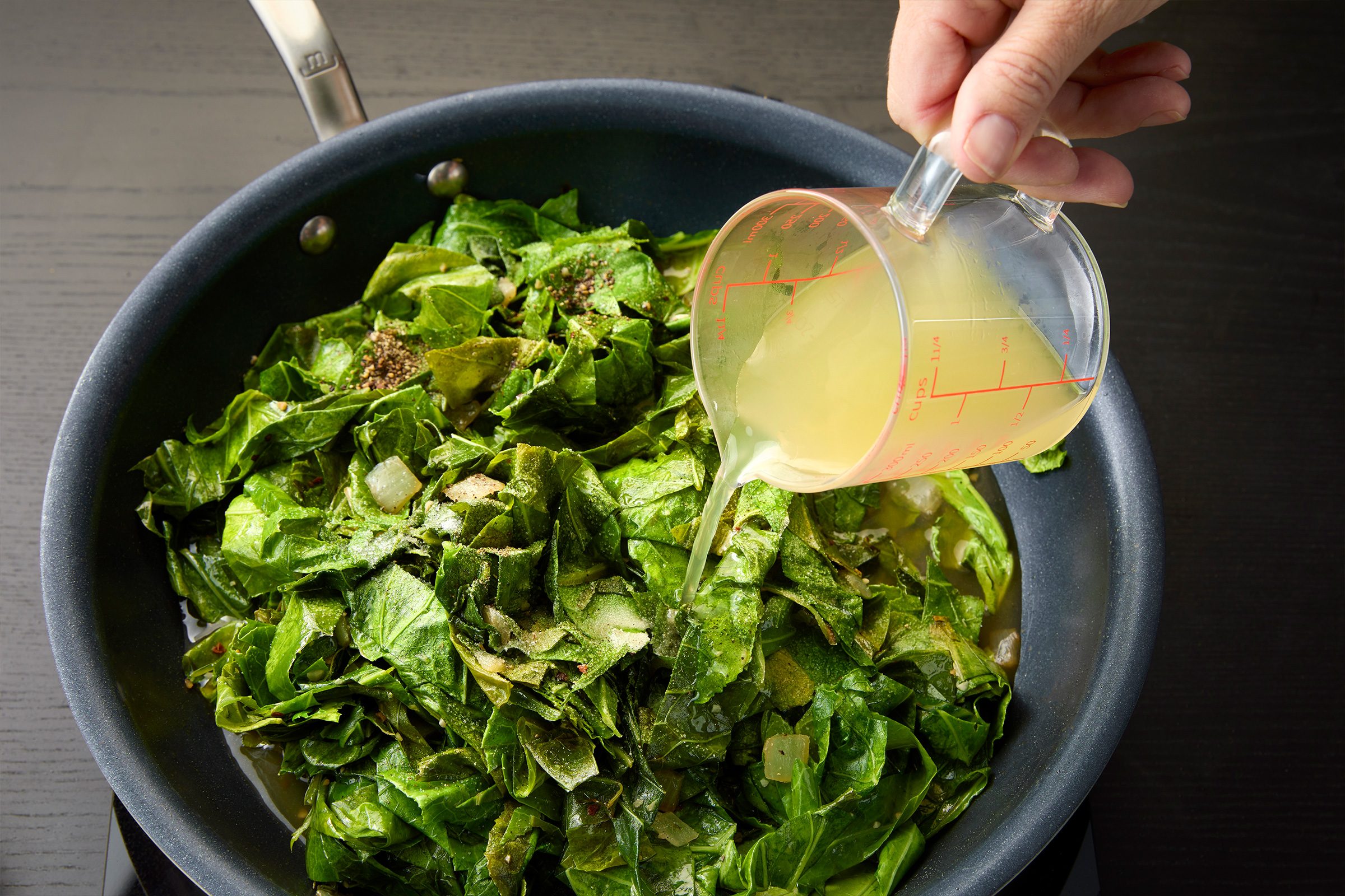 adding the chicken broth, vinegar, salt and pepper to the wilted collard greens