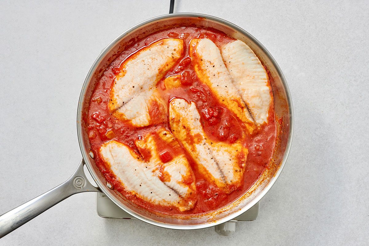 Cooked fish placed on top of the sauce in a skillet
