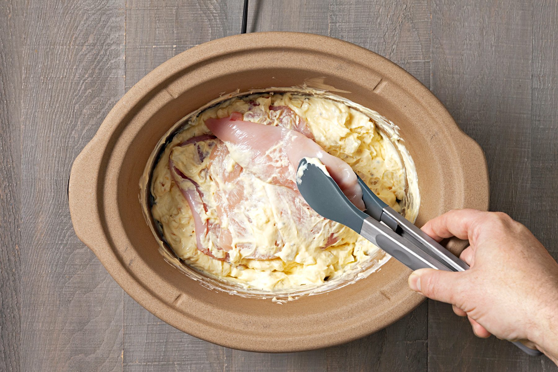 Chicken is being tossed to coat in a slow cooker.
