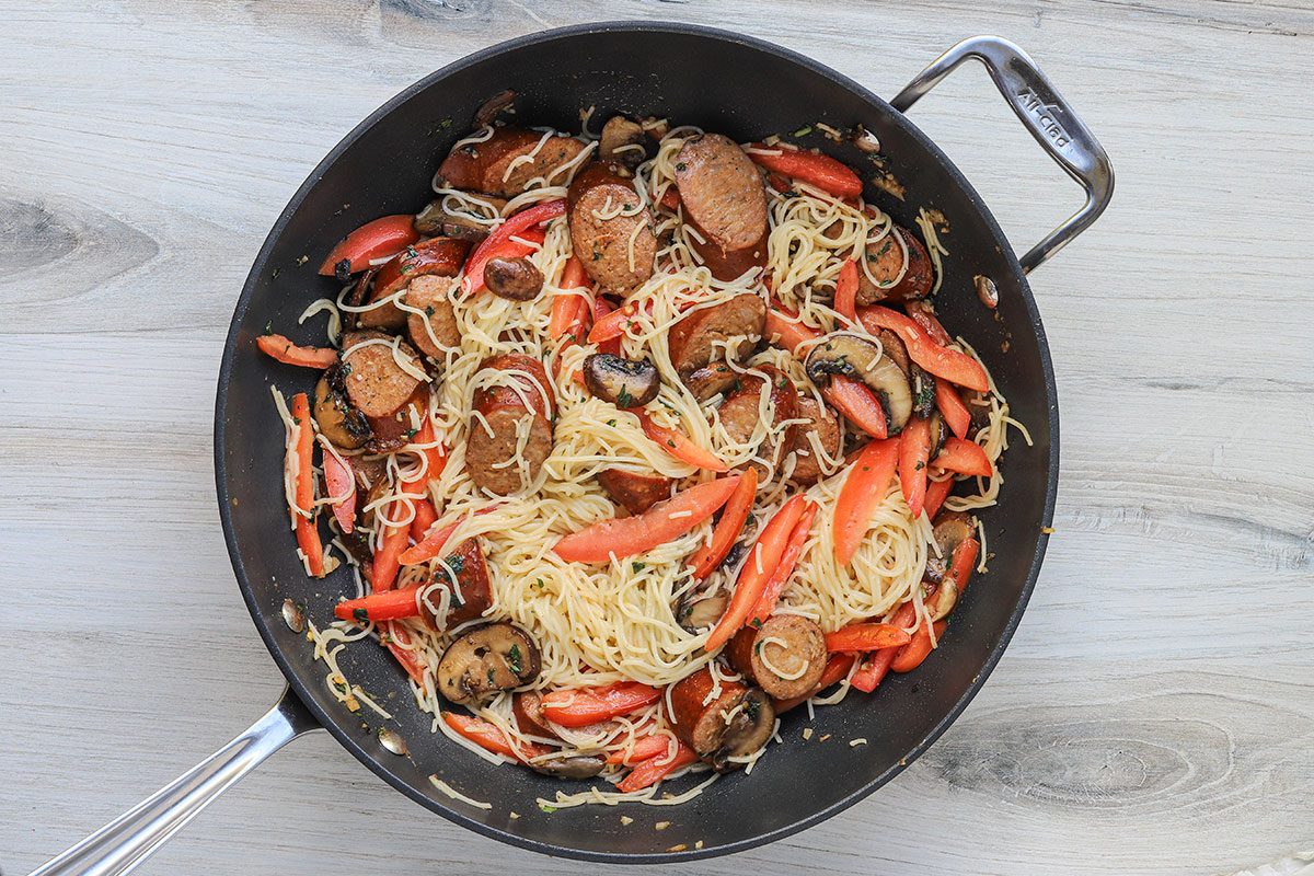 Angel hair pasta and julienned plum tomatoes are added to the smoked sausage mixture in the skillet.