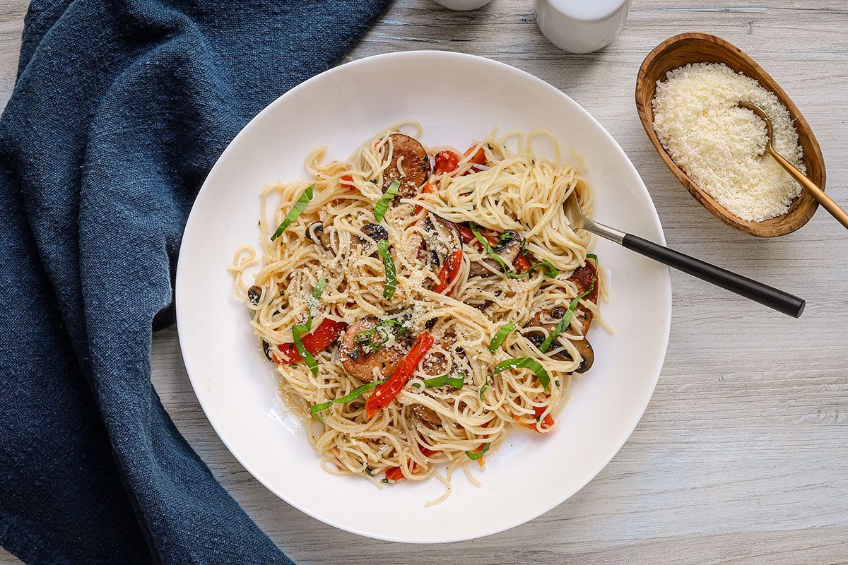 Smoked sausage and pasta meal plated in a pasta bowl with Parmesan cheese on the side.