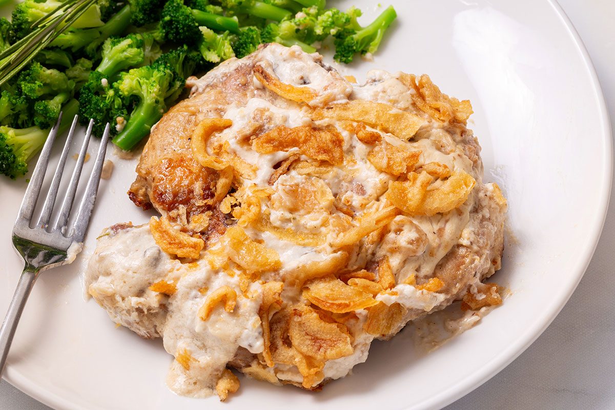 Smothered Pork Chops on a serving plate with a side of broccoli for Taste of Home
