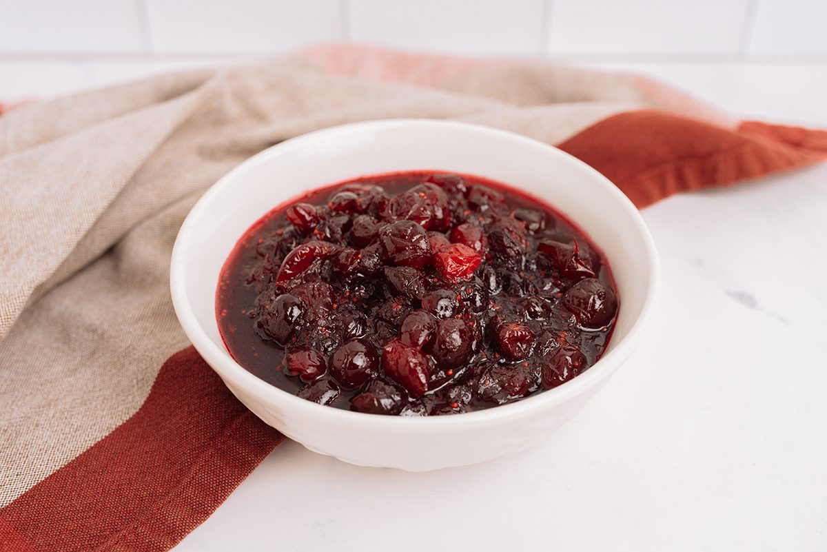 Cranberry sauce in a white bowl with a pink and maroon cloth napkin in the background