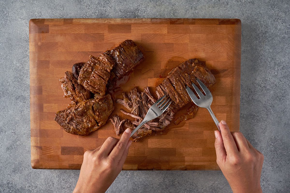 Shred the cooked steaks using two forks and return the shredded beef to the slow cooker to heat through for the Shredded Steak Burritos recipe by Taste of Home.