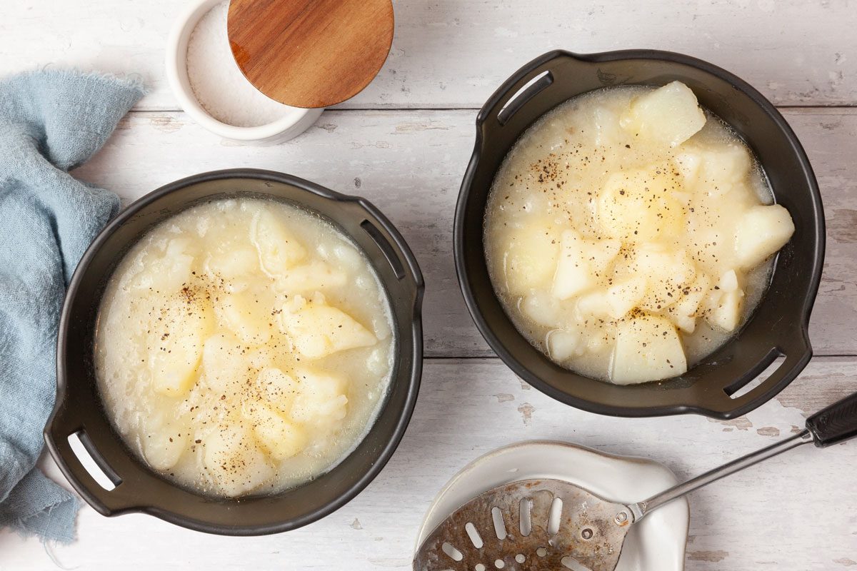 Two servings of Taste of Home Stewed Potatoes in black bowls, topped with pepper