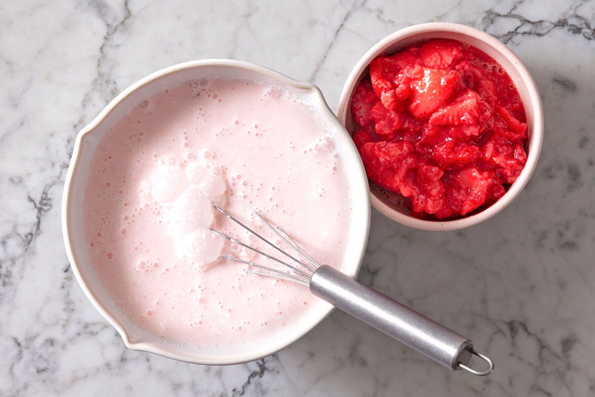 Ice cream ingredients mixed in a large mixing bowl with strawberries nearby