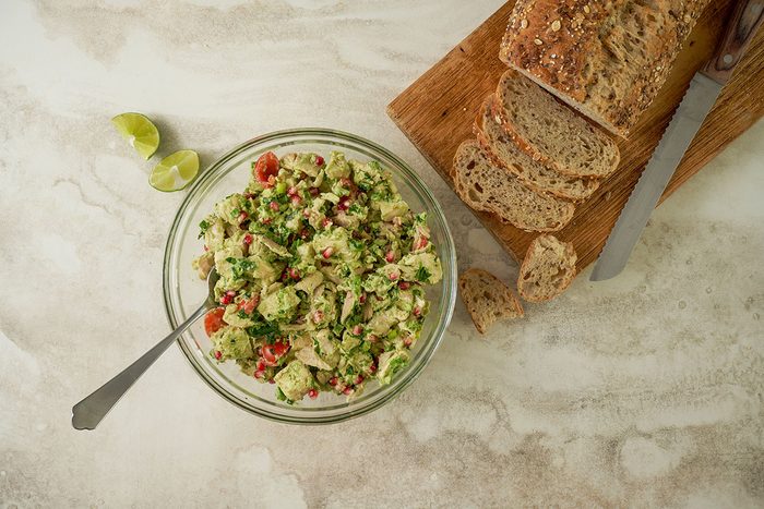 Overhead hero shot of the finished Taste of Home Avocado Chicken Salad, showcasing the vibrant colors of the pomegranate seeds, cherry tomatoes, and cilantro, served in a large bowl.
