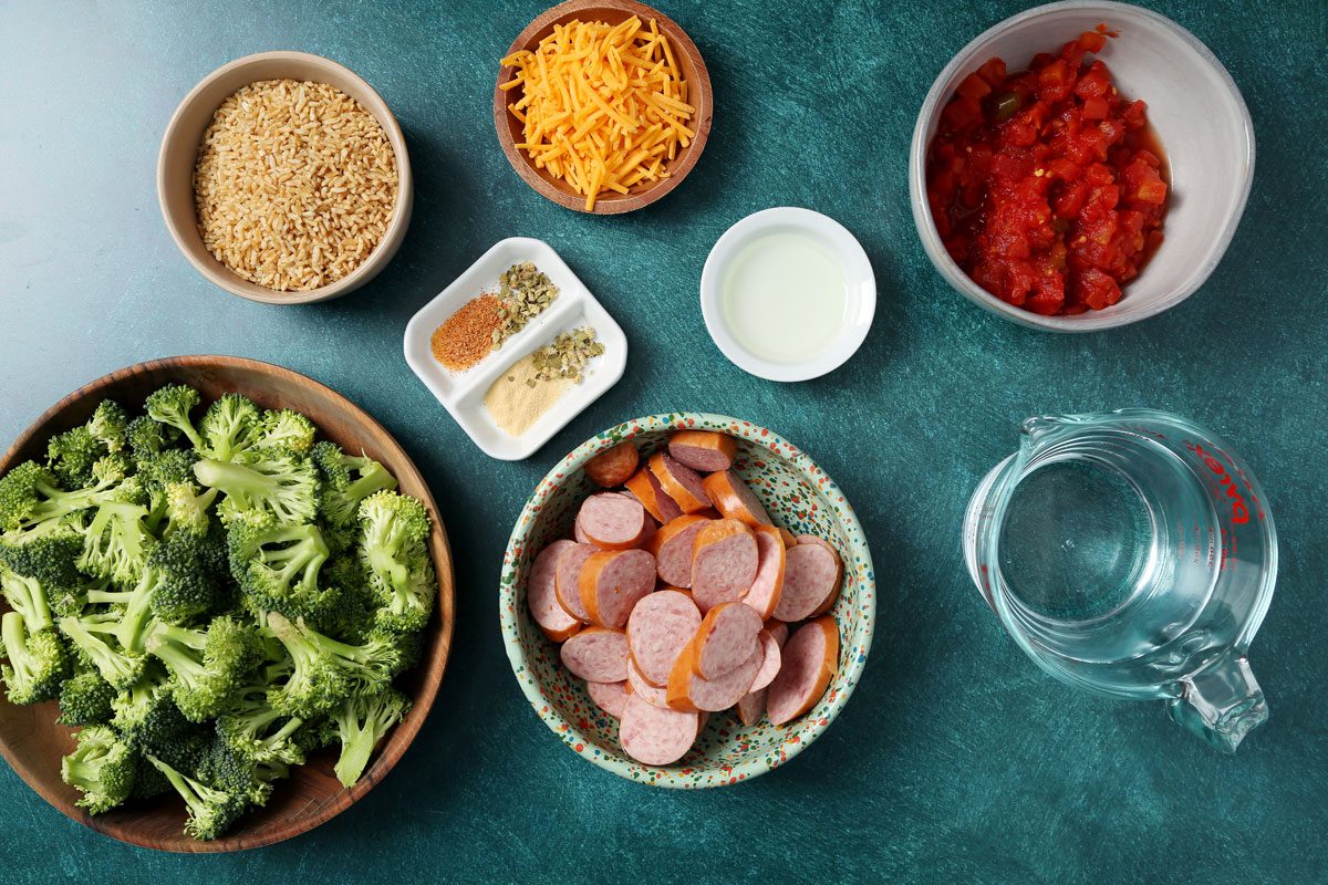 Ingredients for Taste of Home's Sausage, Rice and Broccoli laid out in small bowls on a green surface.