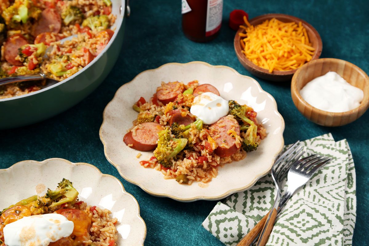 Close up of Taste of Home's Sausage, Rice and Broccoli served on beige plates on a green surface with a green linen.