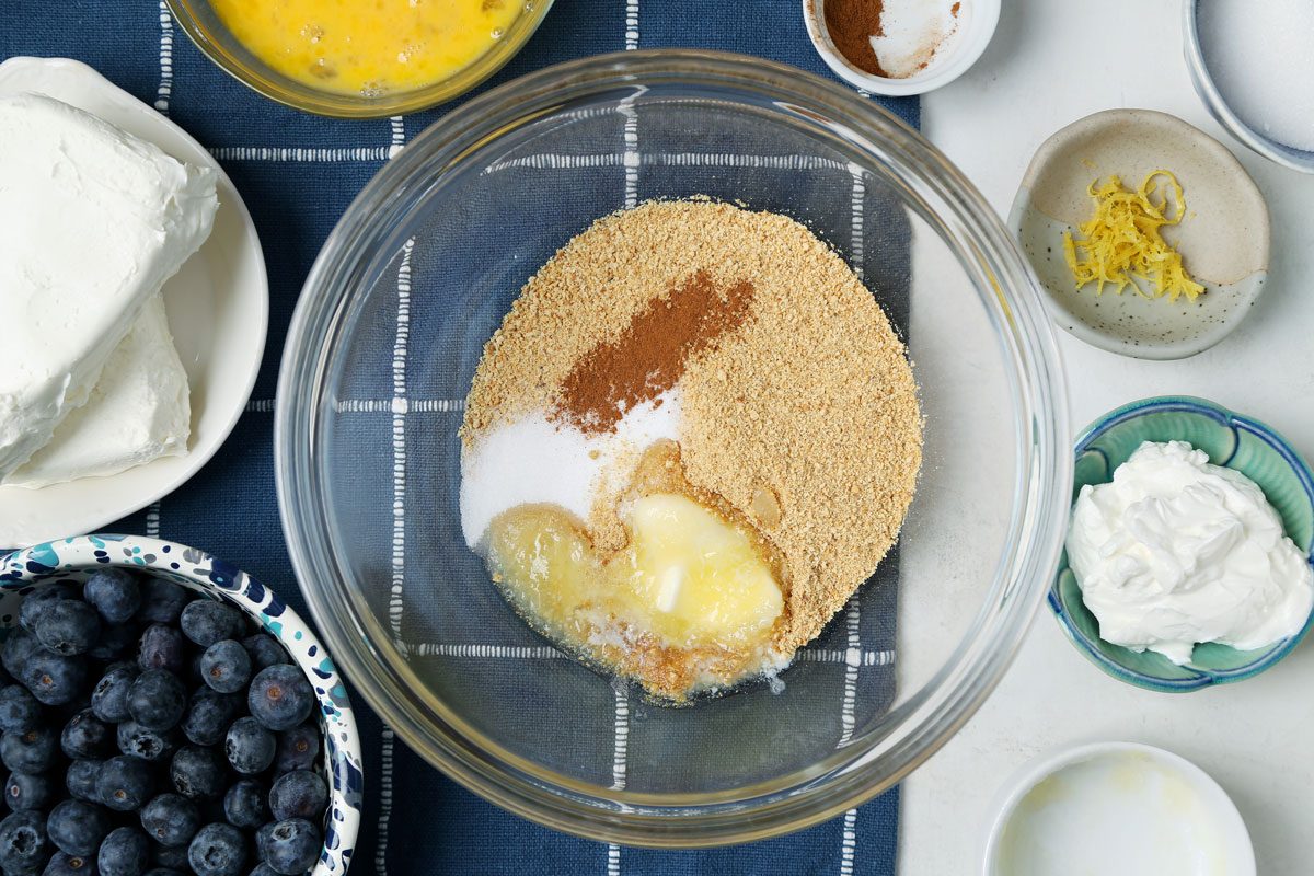 Process of making Taste of Home's Blueberry Cheesecake Bars in a baking dish on a blue linen cloth.