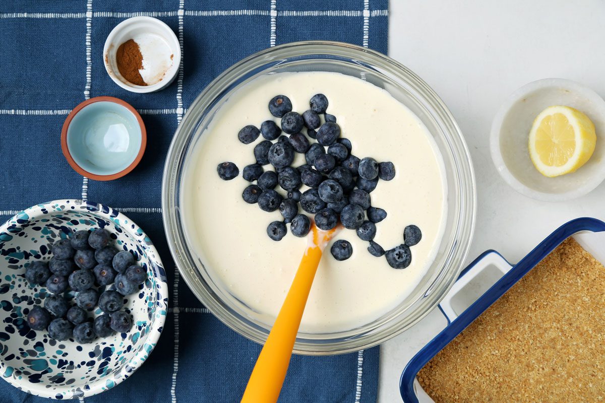 Process of making Taste of Home's Blueberry Cheesecake Bars in a baking dish on a blue linen cloth.