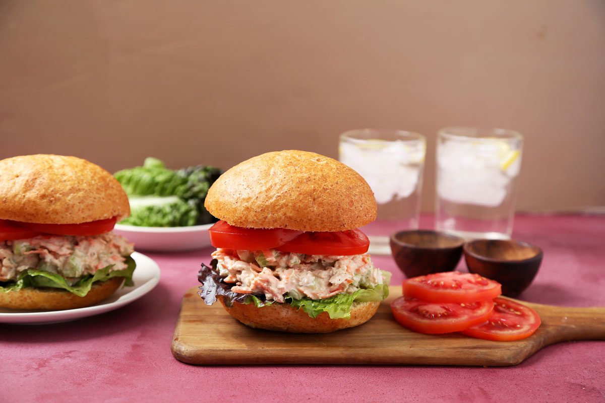Close up of Taste of Home's salmon salad sandwich on a wooden board and a magenta surface.