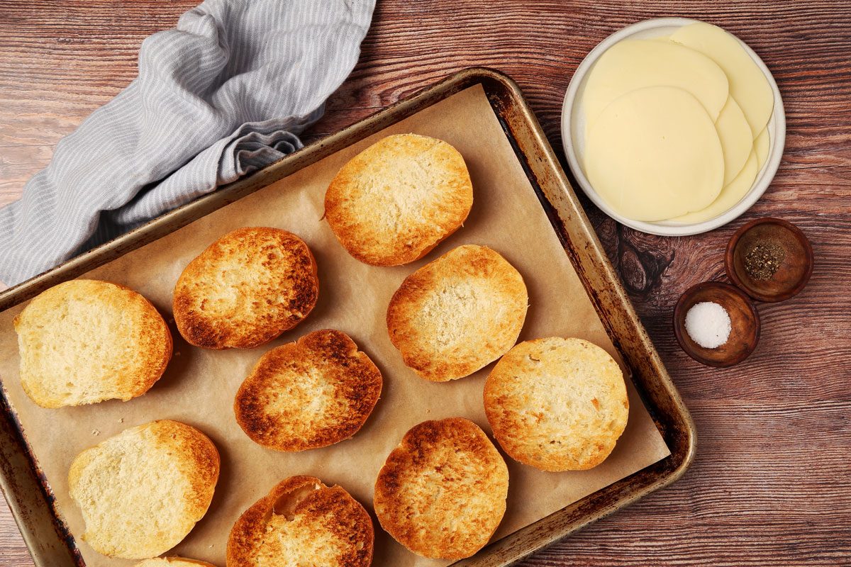 Process of making Taste of Home's Philly Cheesesteak Sloppy Joes on a brown wooden surface. Buns toasted on a baking sheet.