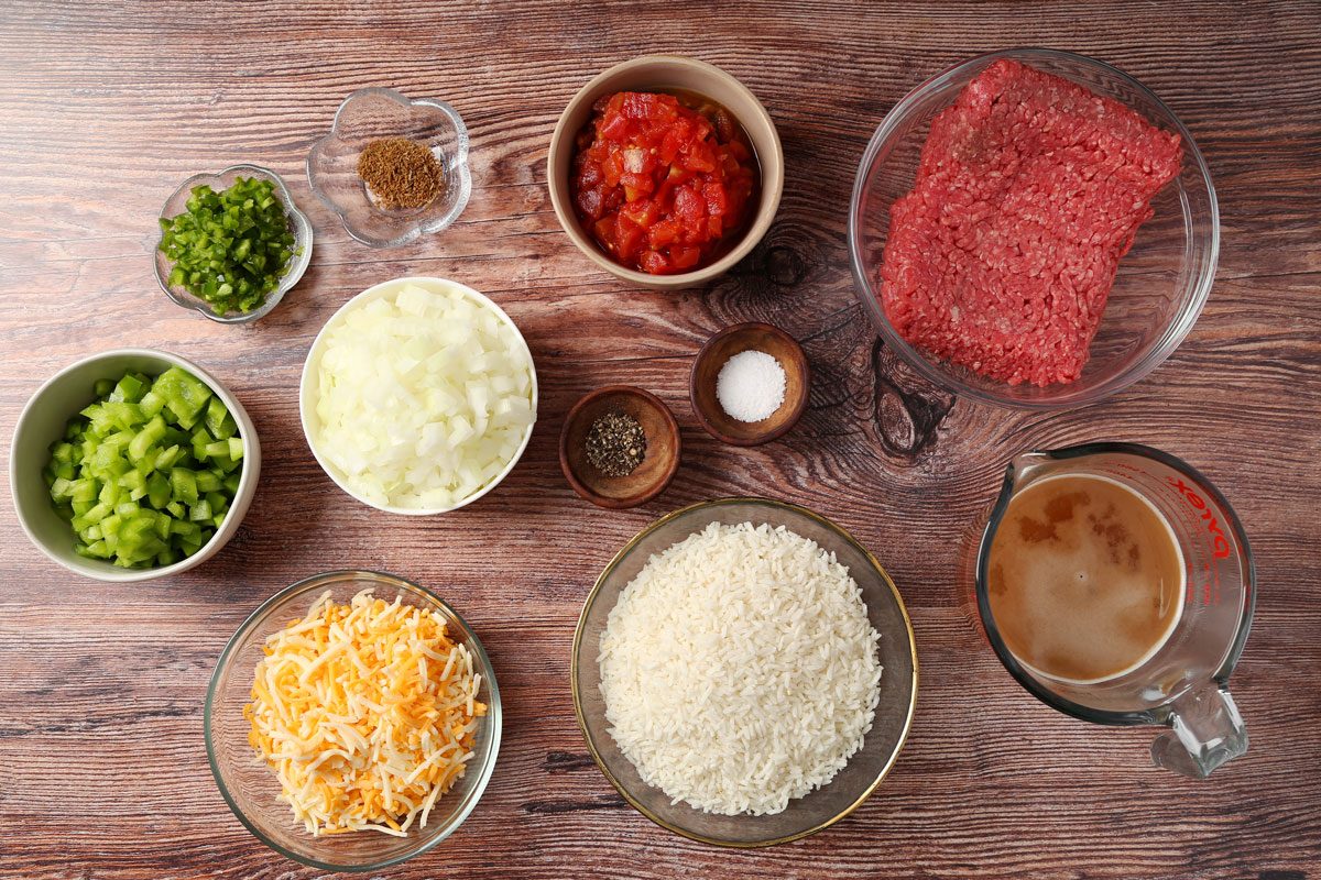 Ingredients for Taste of Home's Beef and Rice Skillet laid out in small bowls on a brown wooden surface.
