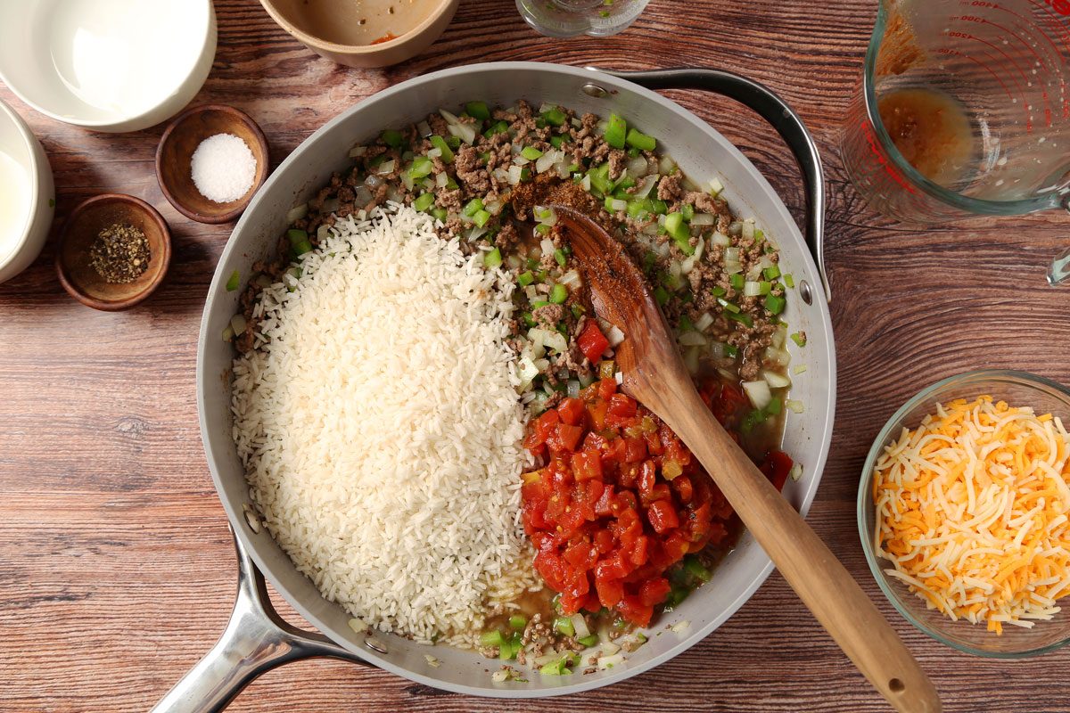 Process of making Taste of Home's Beef and Rice Skillet in a large skillet on a brown wooden surface.