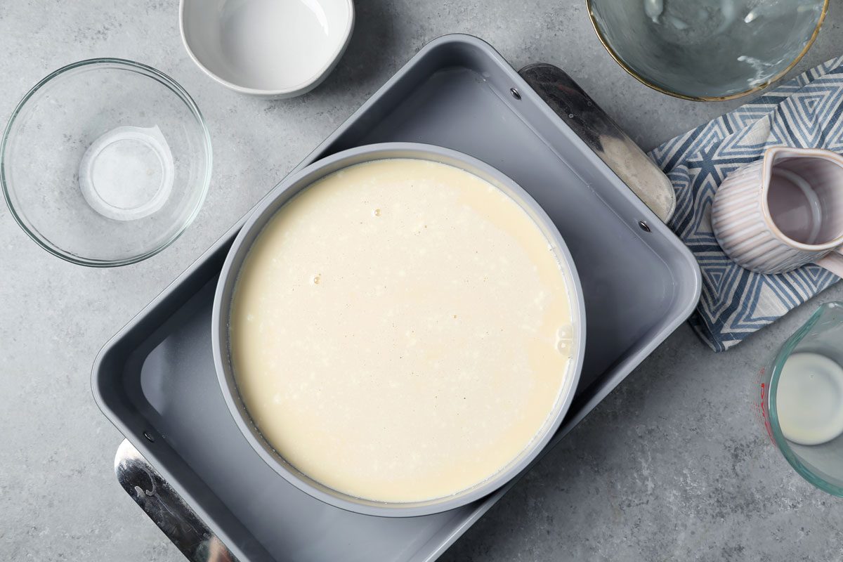 Process of making Taste of Home's Flan de Queso. Flan in a round baking pan in a large roasting pan with water.