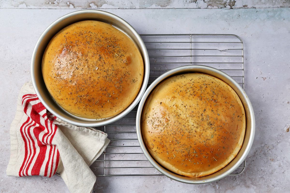Process of making Taste of Home's Italian Sweet Bread loaves cooling on a wire rack on a grey and beige surface.