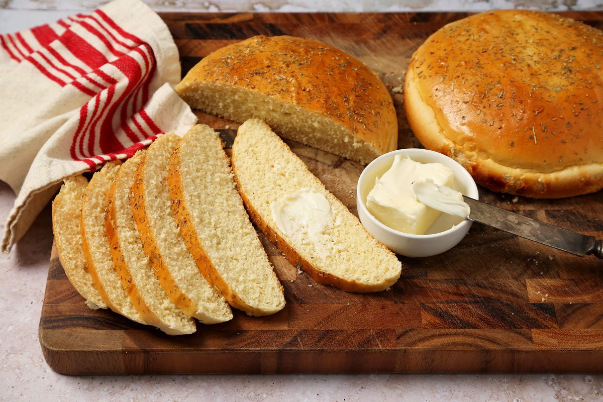 Close up of Taste of Home's Italian Sweet Bread sliced on a wooden cutting board with butter on a grey and beige surface.