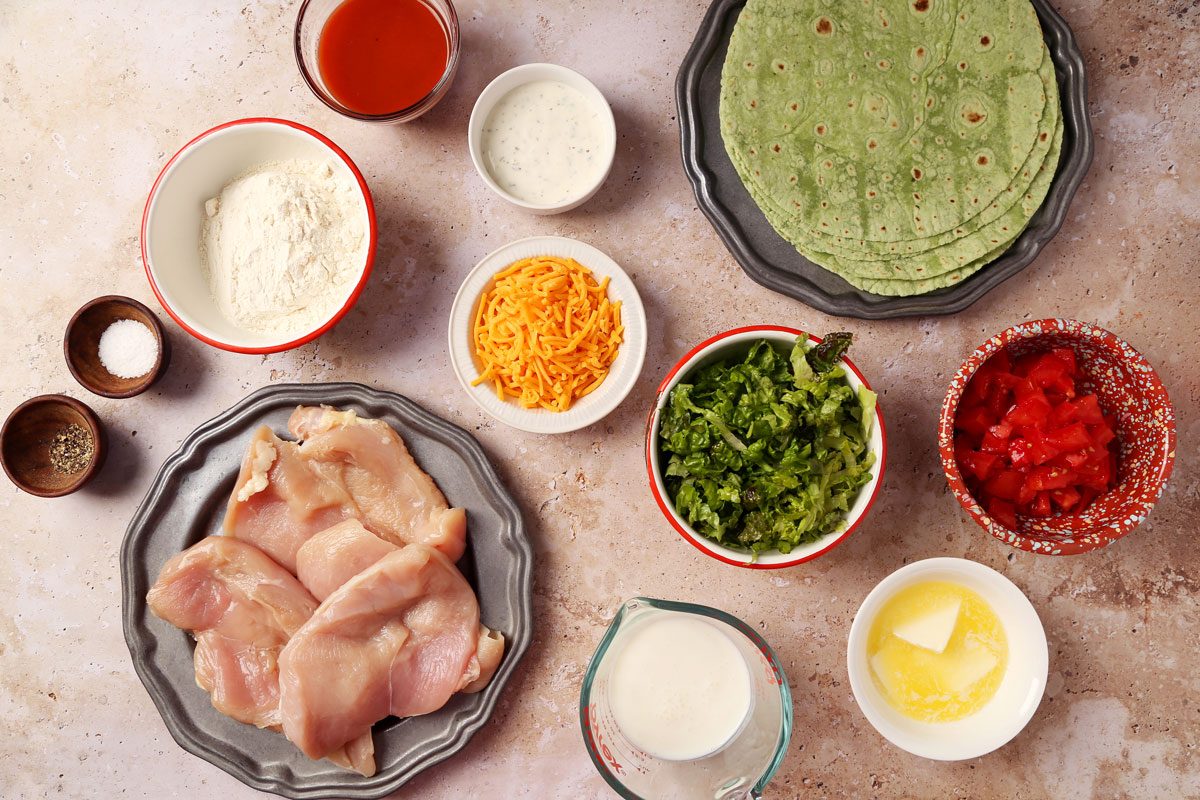 Ingredients for Taste of Home's Buffalo Chicken Wrap laid out in small bowls on a beige marble surface.