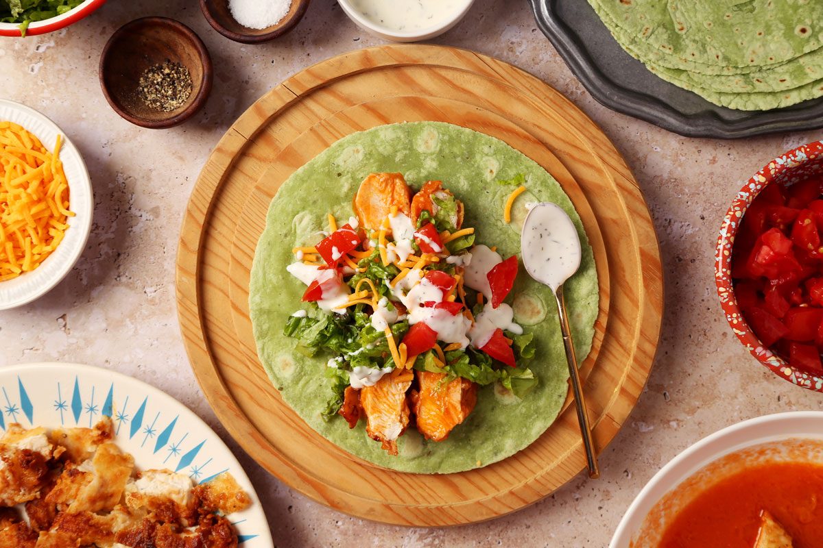 Process of making Taste of Home's Buffalo Chicken Wrap on a wooden serving platter on a beige surface.