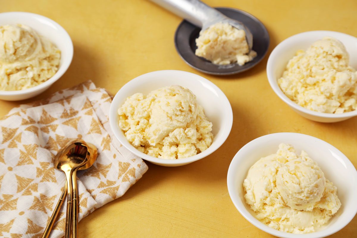 Close up of Taste of Home's Corn Ice Cream scooped and served in small white bowls on a yellow surface.