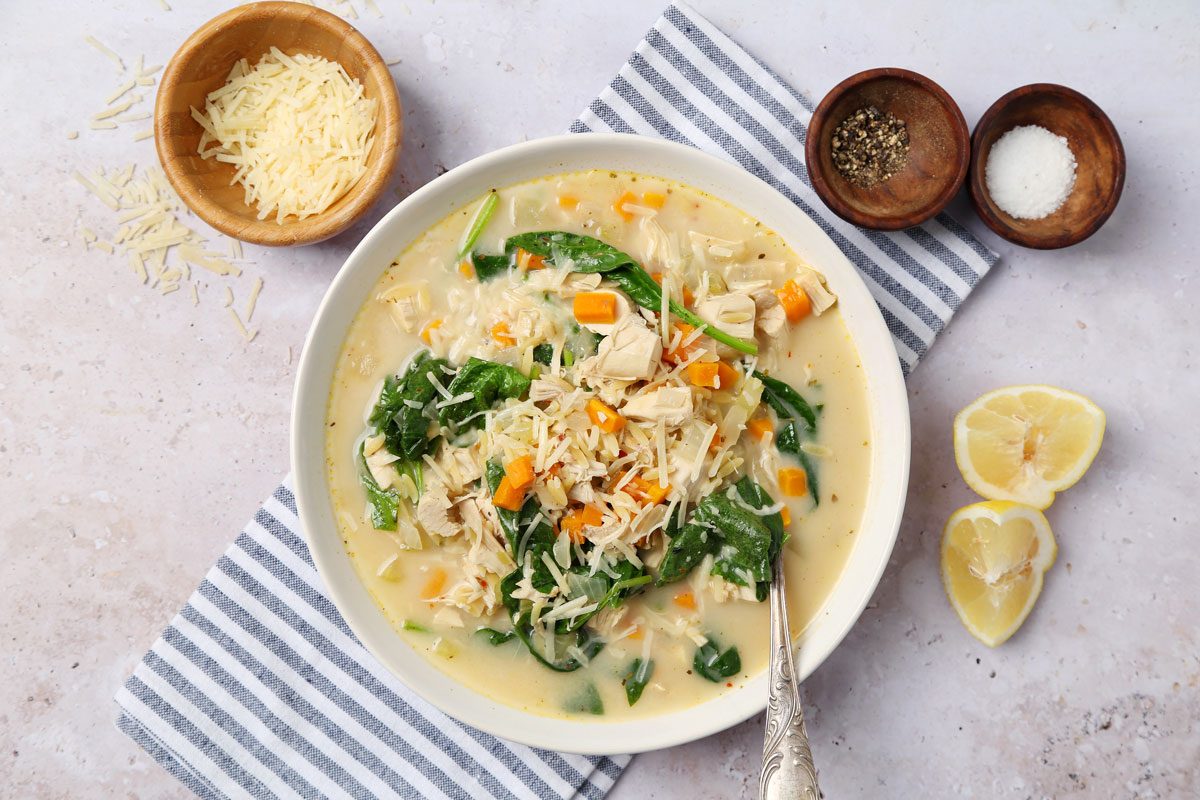 Close up of Taste of Home's Chicken Florentine Soup served in a white bowl on a grey surface.