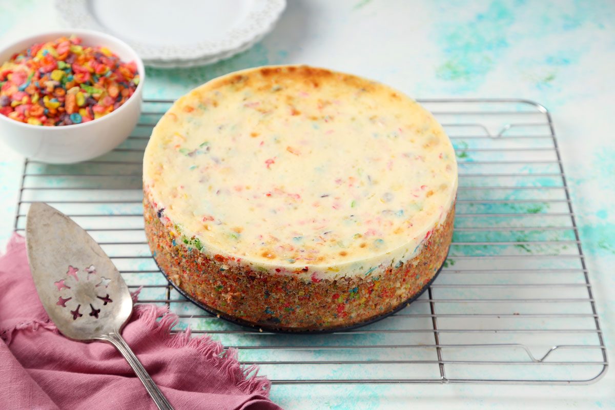 Process of making Taste of Home's Fruity Pebbles Cheesecake being cooled on a wire rack.