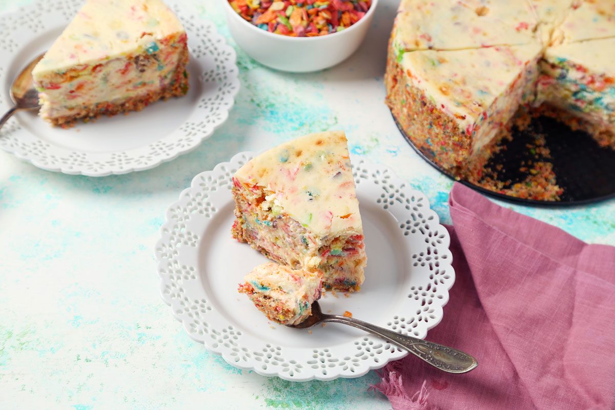 Close up of Taste of Home's Fruity Pebbles Cheesecake sliced and served on a white plate.
