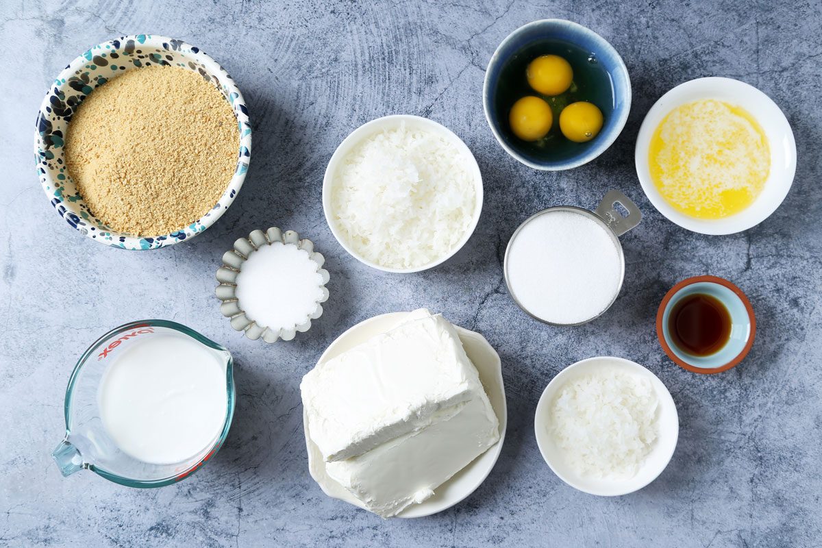 Ingredients for Taste of Home's Coconut Cheesecake laid out in small bowls on a dark blue surface.