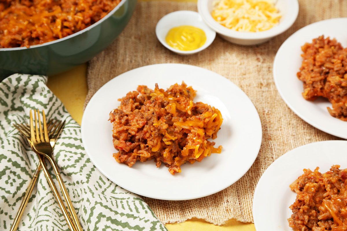 Close up of Taste of Home's Hamburger Casserole served on white plates on a bright yellow surface.