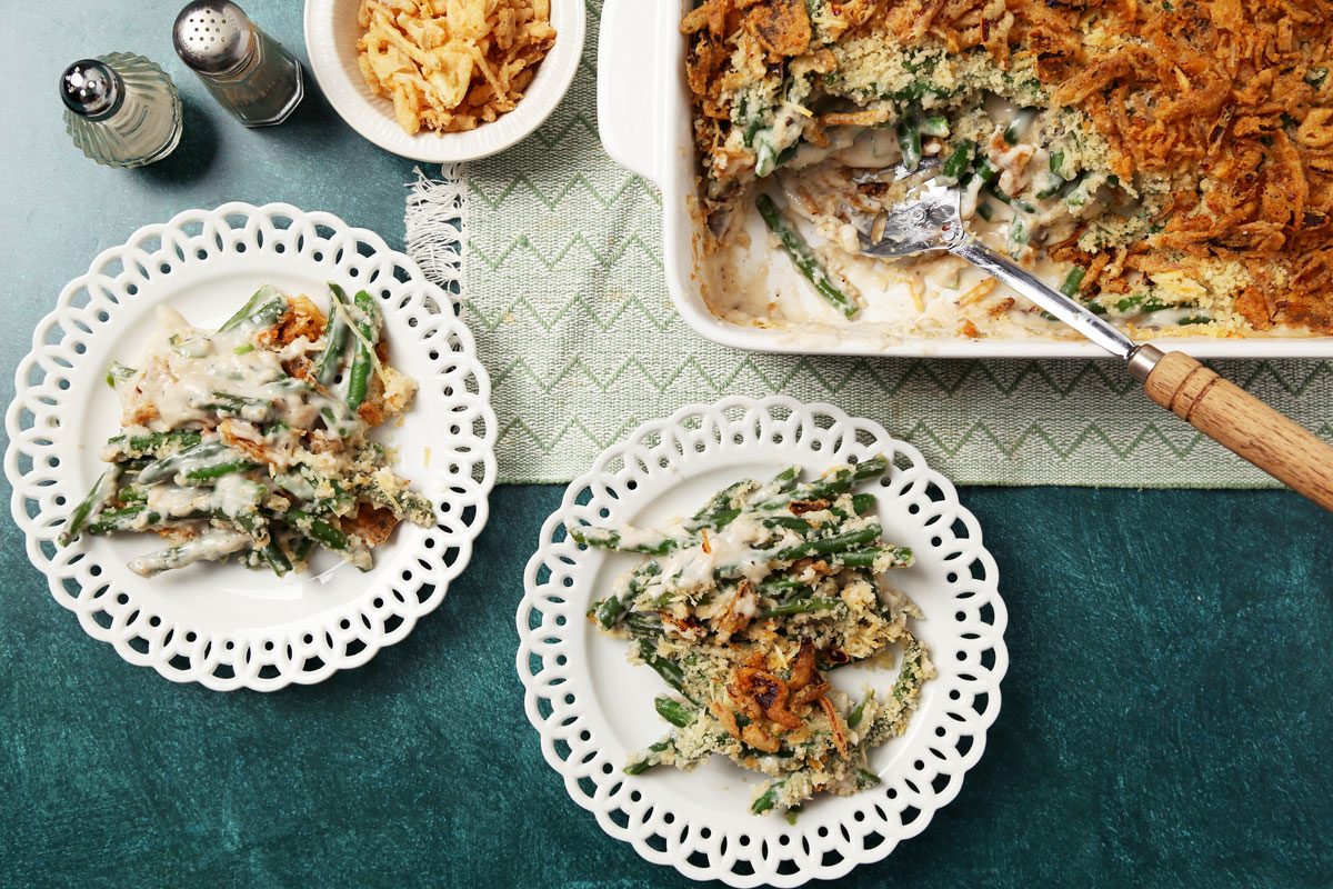 Close up of Taste of Home's Gluten Free Green Bean Casserole served on white lace plates on a teal surface.