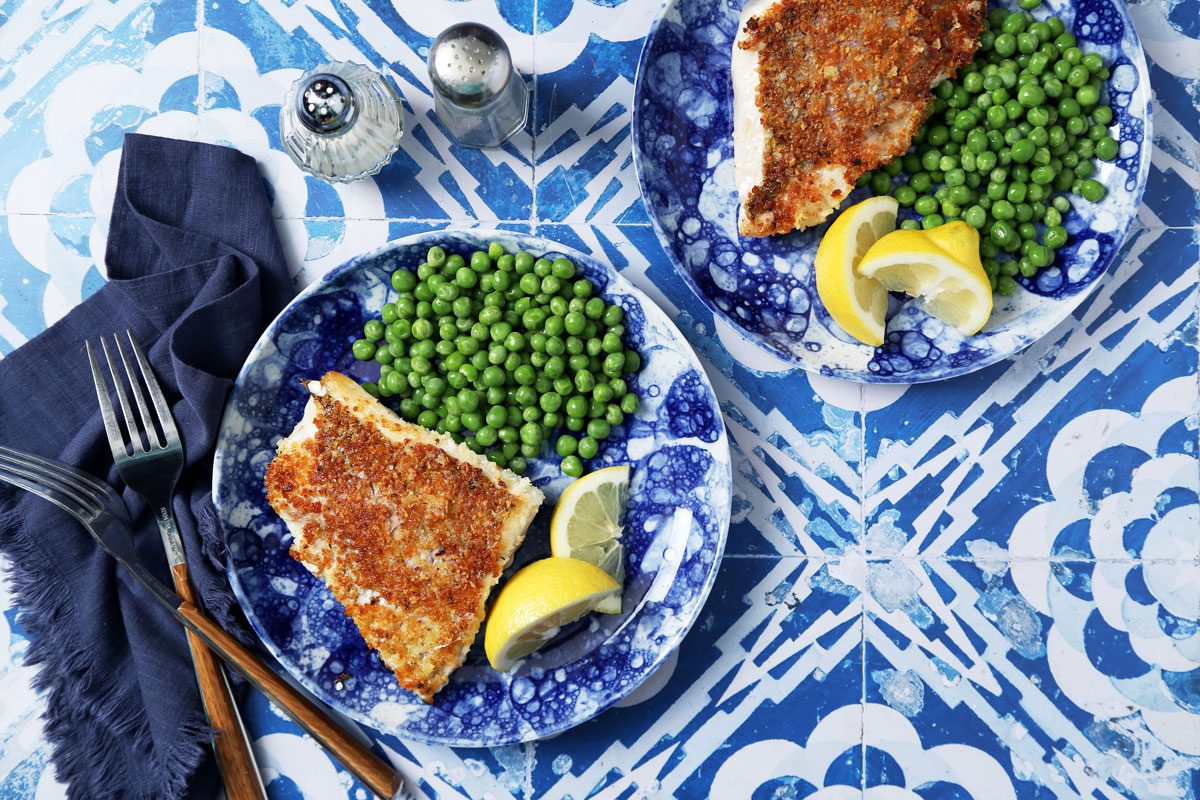 Close up of Taste of Home's Pan-Seared Red Snapper on a blue plate with peas and lemon slices on a blue and white tiled background.