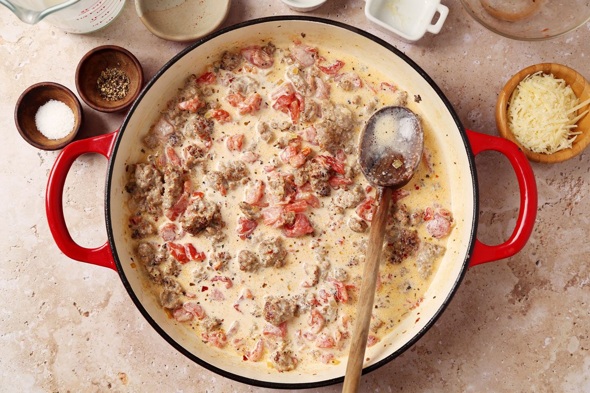 Process of making Taste of Home's Sausage and Bow Tie Pasta laid in a large red dutch oven on a brown marble surface.