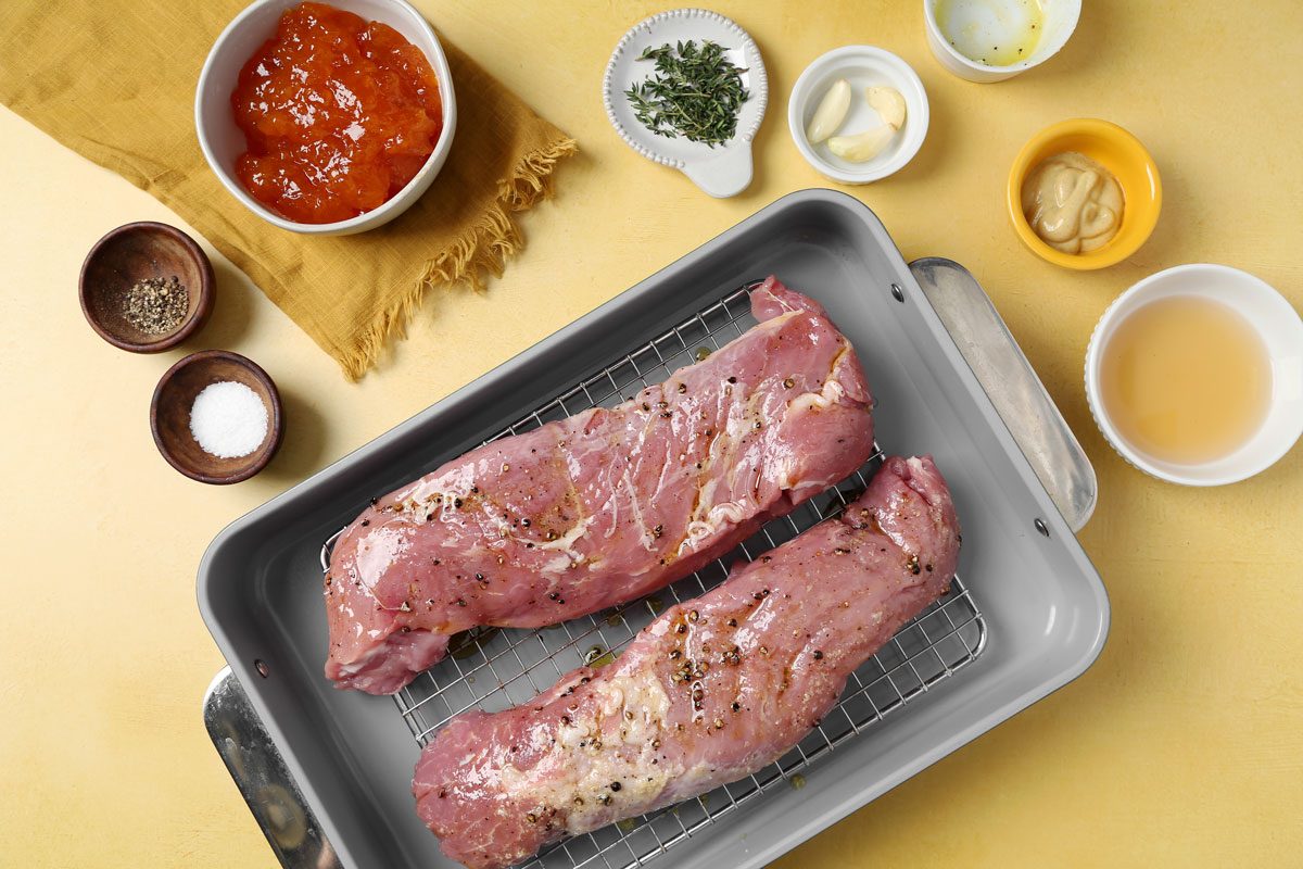 Process of making Taste of Home's apricot glazed pork tenderloin roasting on a roasting rack on a yellow surface.