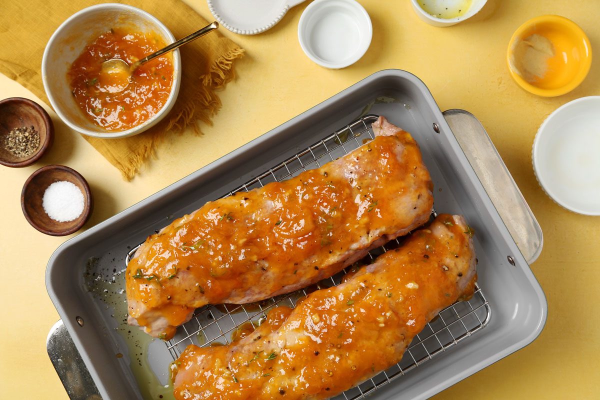 Process of making Taste of Home's apricot glazed pork tenderloin roasting on a roasting rack on a yellow surface.