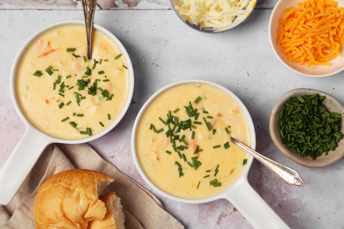 Close up of Taste of Home's Cheddar Cheese Soup served in soup bowls on a grey surface.